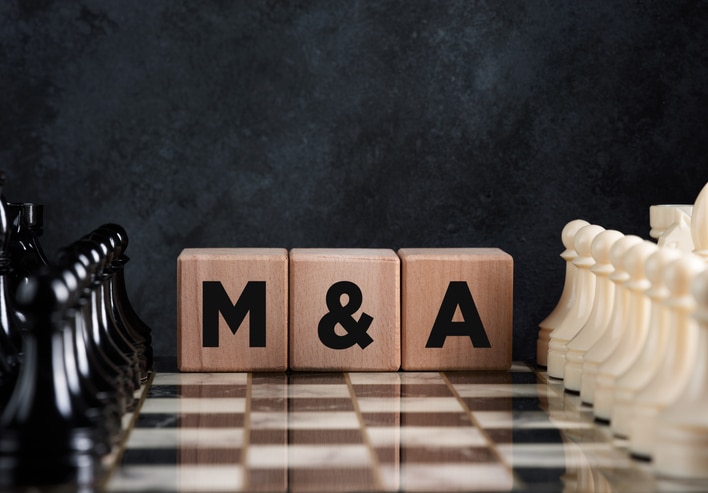 Chessboard with chess pieces and wooden blocks with the word mergers and acquisitions M&A Trends 2025