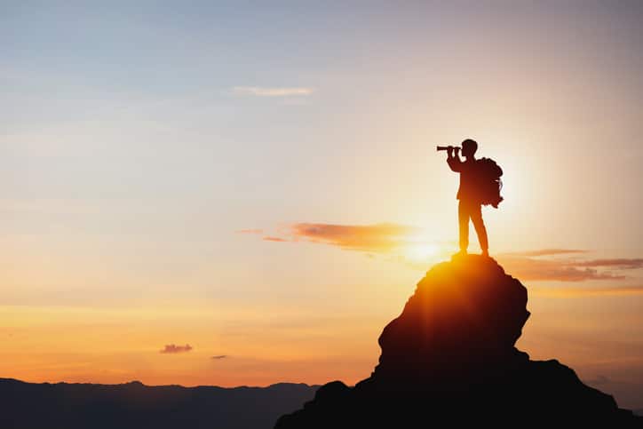 Silhouette of man holding binoculars on mountain peak against bright sunlight sky background. How to Choose a "great" M&A Advisor